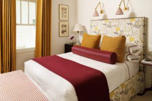 Head and Cheek decided to reuse the bedskirt fabric from a previous design. They then pulled plum and mustard into the soft furnishings such as the curtains and the pillow shams.